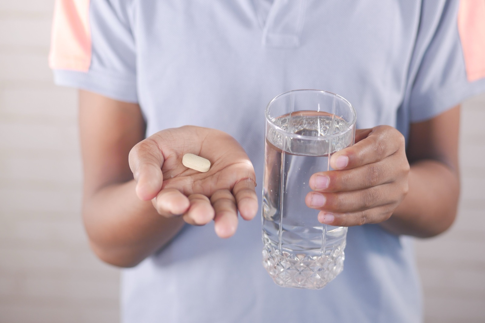 An open hand holding a single white tablet beside a glass of water